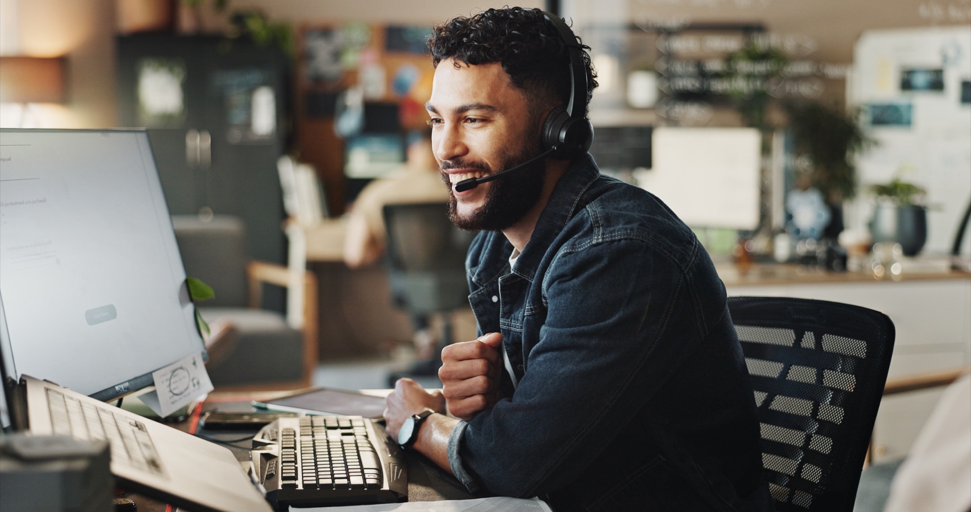 Support engineer wearing a headset, smiling while helping a caller at an office workstation